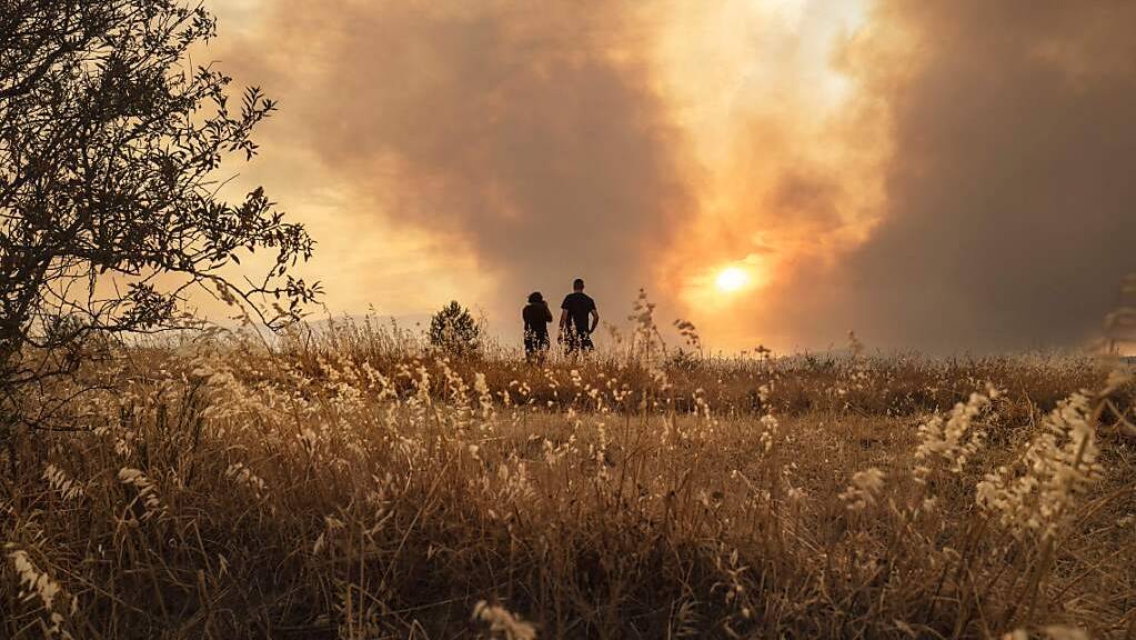 Menschen beobachten einen Waldbrand in Südfrankreich. Im Kampf gegen den Brand zwischen den Städten Narbonne und Carcassonne sind über 1000 Feuerwehrleute und Retter im Einsatz. Foto: Idriss Bigou-Gilles/AFP/dpa