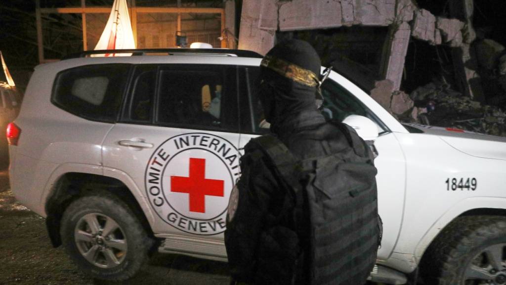 ARCHIV - Ein bewaffneter Mann in der Uniform der al-Qassam-Brigaden, dem militärischen Flügel der Hamas, steht Wache, als Fahrzeuge des Roten Kreuzes ein Lagerhaus verlassen. In dem Lagerhaus sollen angeblich Särge mit den Leichen von vier verstorbenen Geiseln abgeholt und nach Israel gebracht werden. Foto: Yousef Al Zanoun/AP/dpa