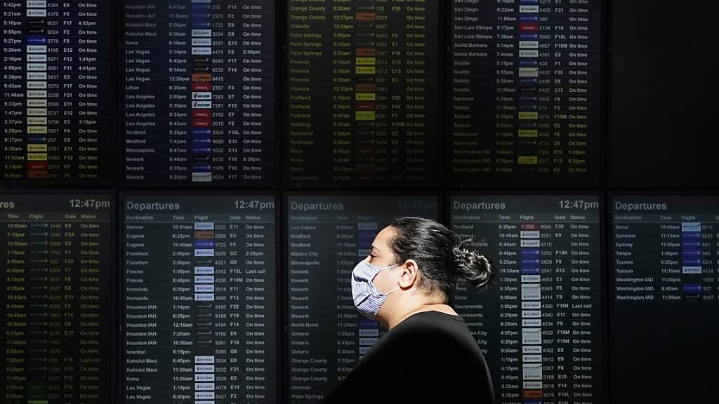 ARCHIV - Eine Frau mit Mund-Nasen-Schutz geht an einer Anzeigetafel am Internationalen Flughafen von San Francisco vorbei. Foto: Jeff Chiu/AP/dpa