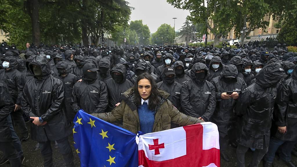 ARCHIV - Eine Frau mit einer georgischen Nationalfahne und einer EU-Fahne steht vor Polizisten, die eine Straße sperren, um Demonstranten während eines Protestes der Opposition gegen das «Russische Gesetz» in der Nähe des Parlamentsgebäudes aufzuhalten. Foto: Zurab Tsertsvadze/AP/dpa
