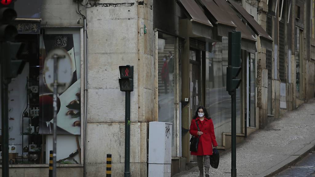 ARCHIV - Eine Frau mit Maske geht eine sehr ruhige Straße in der Innenstadt entlang. Foto: Armando Franca/AP/dpa
