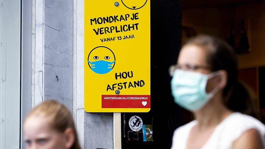Eine Frau mit Mundschutz geht an einem Schild mit Informationen über die Maskenpflicht vorbei. Das Tragen eines Mund-Nasen-Schutzes aufgrund des Coronavirus ist an belebten Orten in Amsterdam Pflicht. Foto: sem Van Der Wal/ANP/dpa