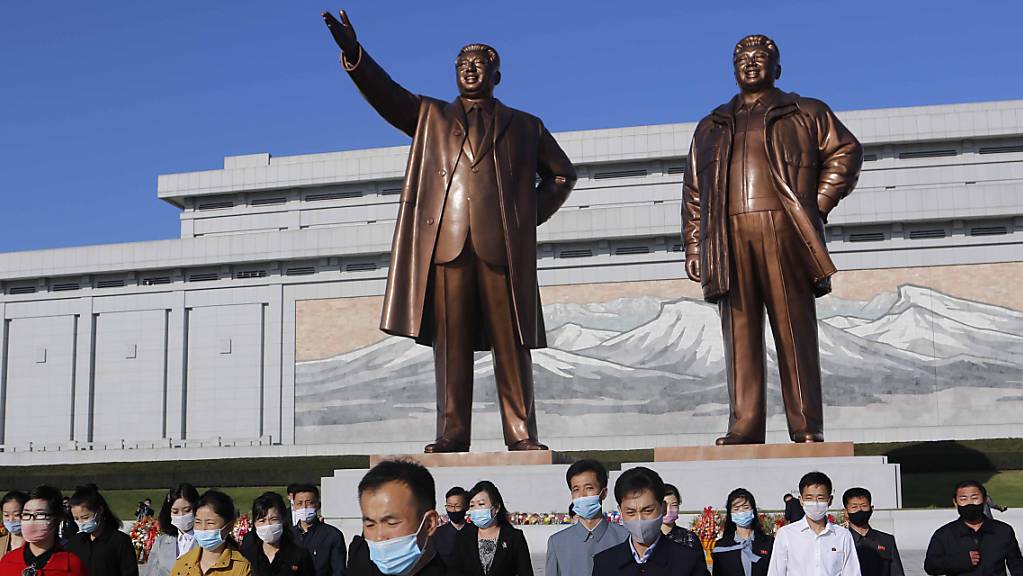 Menschen mit Maske besuchen den Mansu-Hügel, um vor dem Grossmonument Mansudae, welches die zwei verstorbenen nordkoreanischen Machthaber Kim Il-sung (l) und Kim Jong-il zeigt, anlässlich des 75. Jahrestages der Gründung der Arbeiterpartei des Landes, Blumen niederzulegen. Foto: Cha Song Ho/AP/dpa