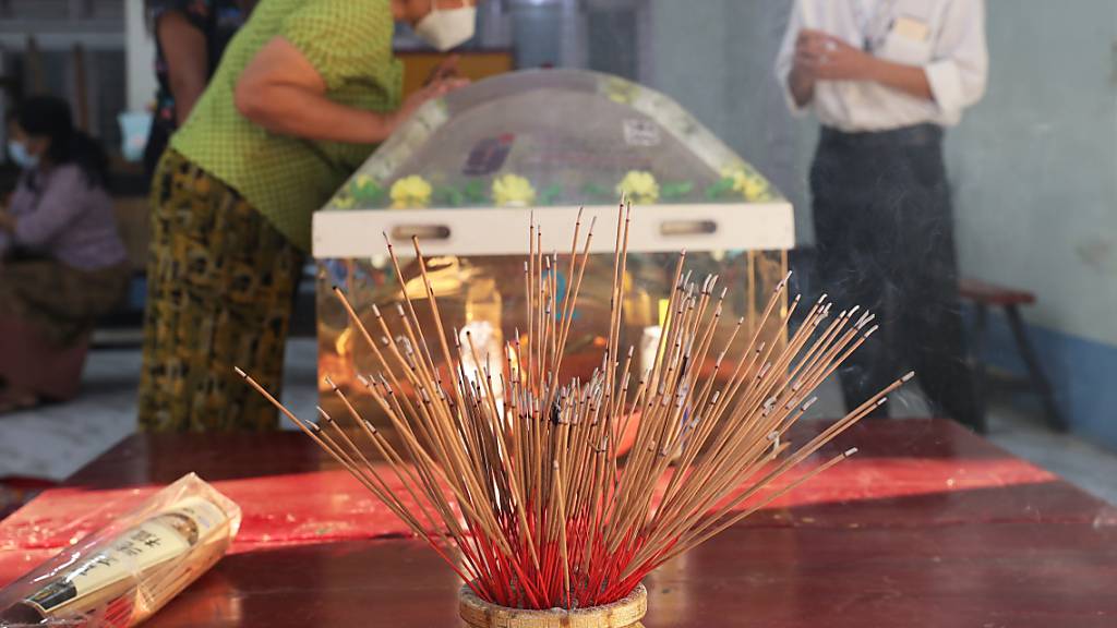 Angezündete Weihrauchstäbchen stehen auf einem Tisch im chinesischen Yunnan-Tempel, während Menschen den Leichnam von Kyal Sin betrachten. Die 20-jährige Studentin wurde während einer Demonstration gegen den Putsch der Militärjunta von Polizisten mit einem Kopfschuss getötet. Foto: Uncredited/AP/dpa