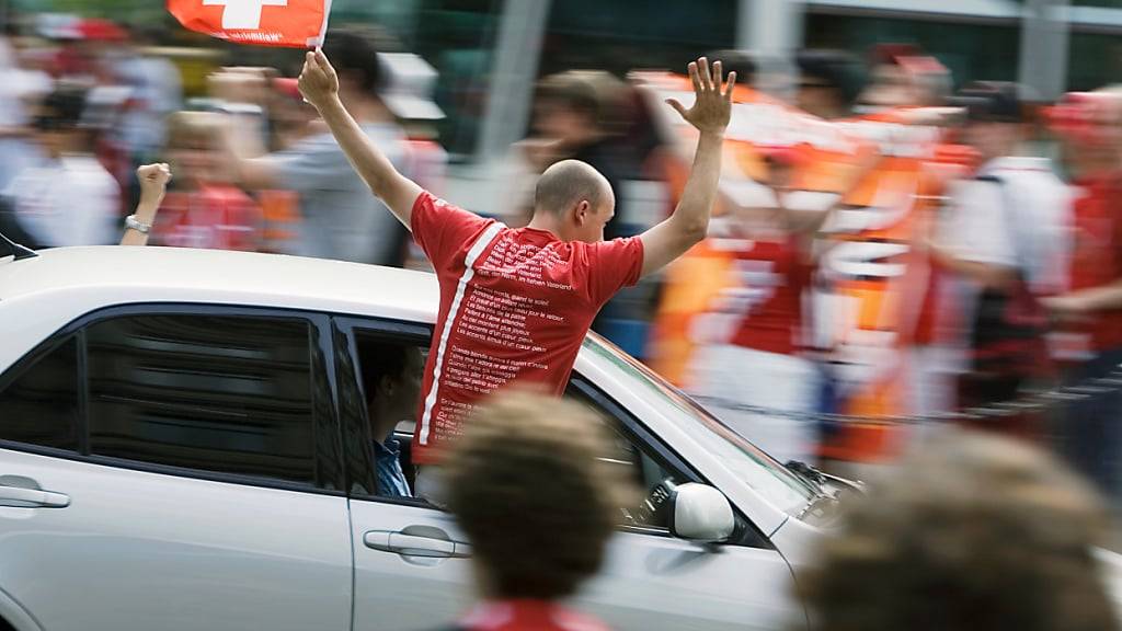 Ein feiernder Fussballfan lehnt sich während der Fahrt aus dem Auto und risikiert eine Anzeige. (Archivbild)