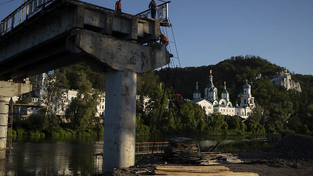Bauarbeiter steigen von einer Leiter auf einer zerstörten Brücke neben dem Kloster Swjatohirsk herunter. Foto: Bram Janssen/AP/dpa