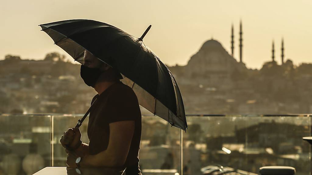 Ein Tourist trägt einen Mund-Nasen-Schutz und hält einen Regenschirm, während er von der Süleymaniye-Moschee über die Stadt blickt. (Archivbild)