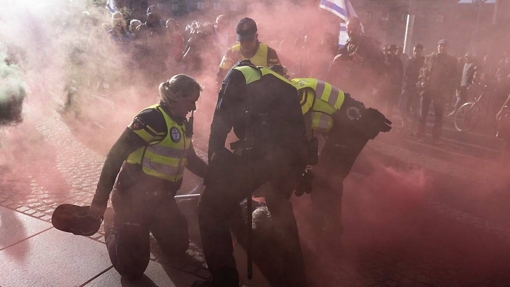 Ein pro-palästinensischer Demonstrant mit einer Rauchbombe wird in Amsterdam von der Polizei festgehalten. Foto: Peter Dejong/AP