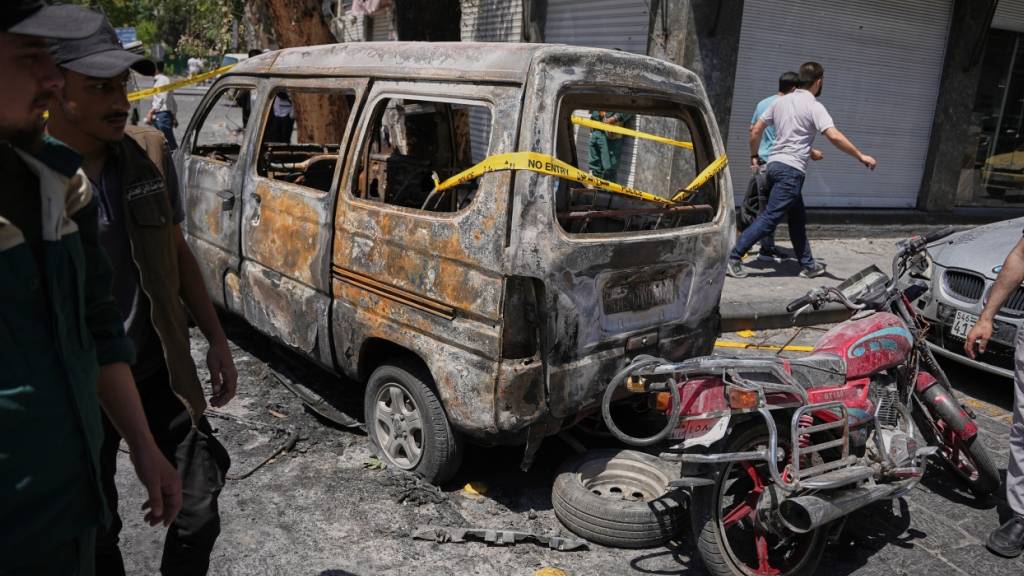 Syrische Sicherheitskräfte untersuchen ein ausgebranntes Fahrzeug in Damaskus, nachdem zuvor zwei Explosionen die Gegend erschüttert hatten. Foto: Omar Albam/AP/dpa