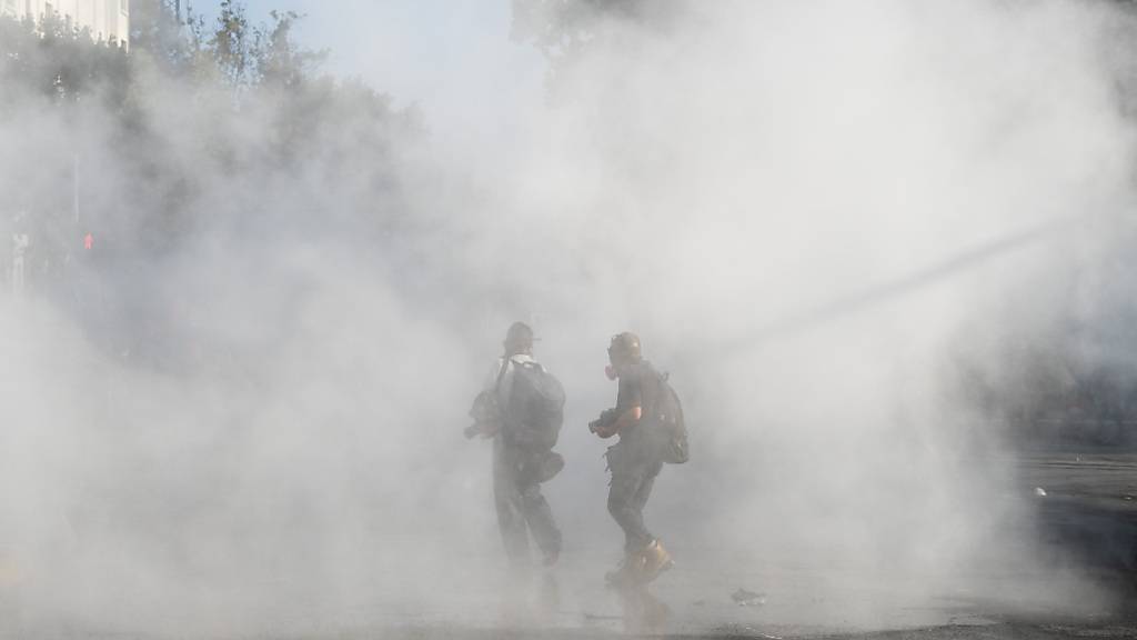 Zwei Personen stehen in einer dichten Tränengaswolke. Nach tödlichen Schüssen eines Polizisten auf einen Straßenkünstler ist es zu heftigen Ausschreitungen gekommen. Foto: Matias Basualdo/ZUMA Wire/dpa