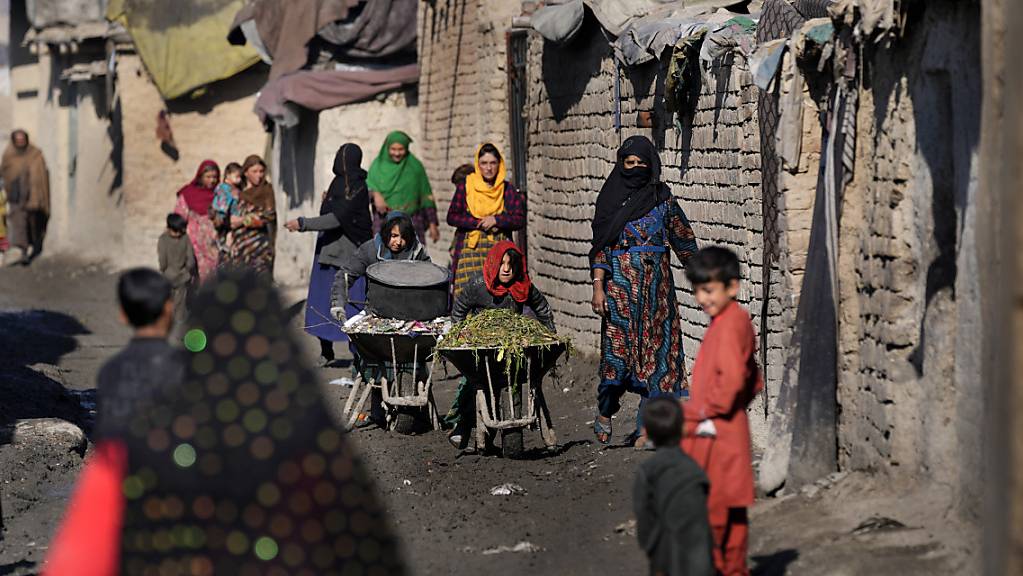 Frauen und Kinder schieben Schubkarren und gehen eine schlammige Gasse in einem Armutsviertel von Kabul entlang. In Afghanistan leiden nach Angaben der Vereinten Nationen am Dienstag mittlerweile 23 Millionen Menschen unter «akutem Hunger» - mehr als die Hälfte der Bevölkerung. 