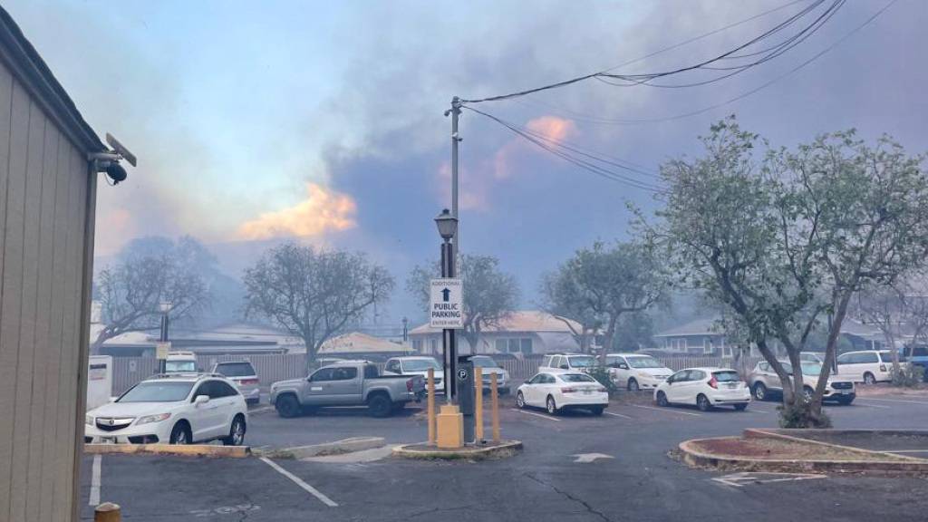 HANDOUT - Autos stehen auf einem Parkplatz in Lahaina, Hawaii während dahinter schon die Flammen hoch schlagen. Foto: Anatol Eisele/dpa - ACHTUNG: Nur zur redaktionellen Verwendung im Zusammenhang mit der aktuellen Berichterstattung und nur mit vollständiger Nennung des vorstehenden Credits