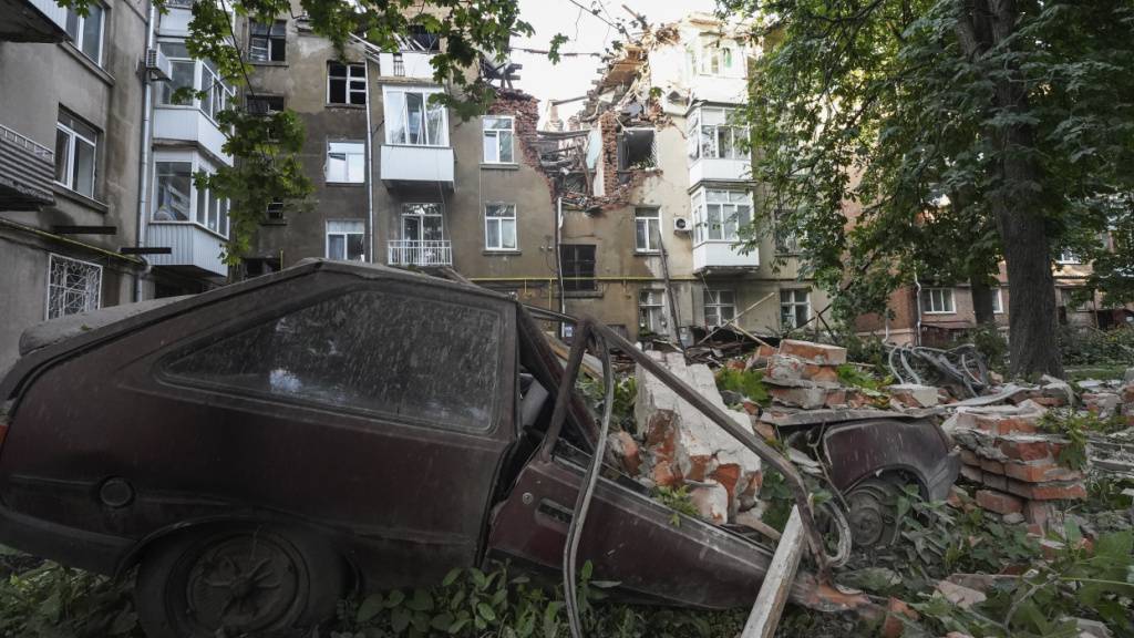 ARCHIV - Ein Autowrack ist nach einem Angriff vor einem beschädigten Wohnhaus in Sumy zu sehen. Foto: Andrii Marienko/AP/dpa/Archivbild