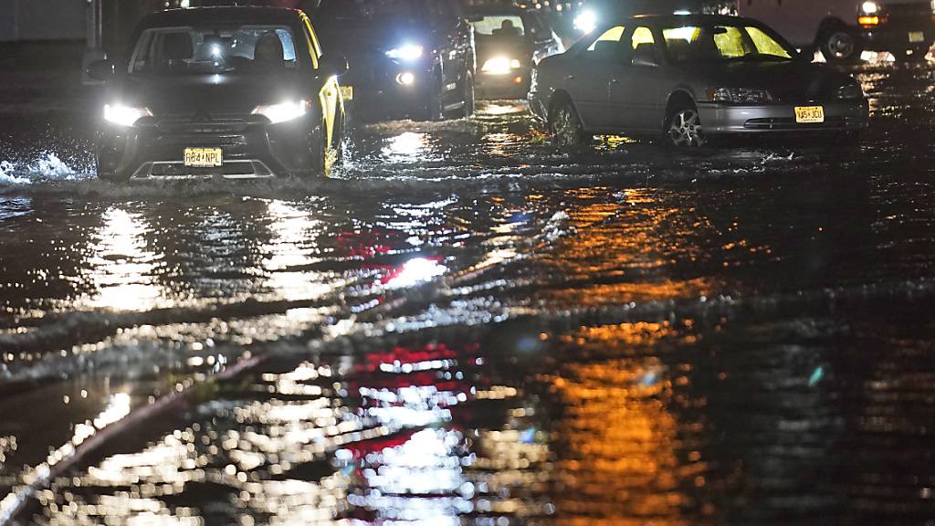 Autos bahnen sich ihren Weg durch New Jersay über überflutete Straßen und an verlassenen Autos vorbei. Foto: Seth Wenig/AP/dpa