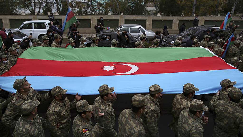 Aserbaidschanische Soldaten tragen eine große Fahne in den Farben ihrer Nationalflagge, während sie die Rückgabe der Region Latschin feiern. Foto: Emrah Gurel/AP/dpa