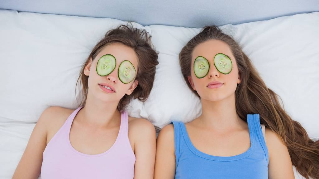Friends relaxing in bed with cucumber on eyes at sleepover