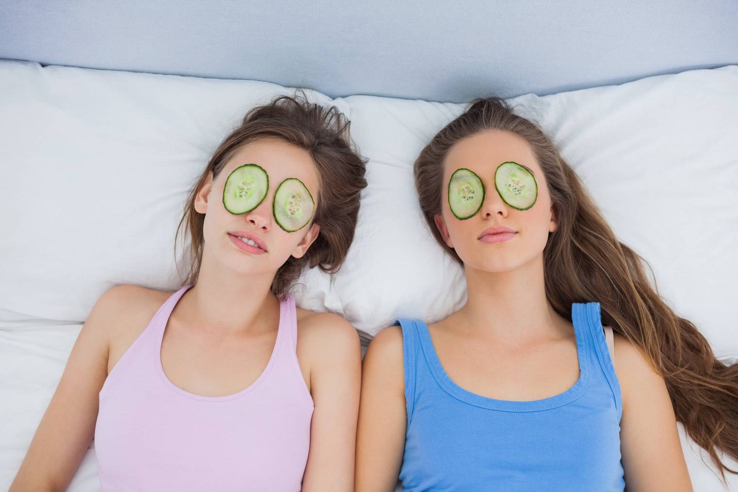 Friends relaxing in bed with cucumber on eyes at sleepover