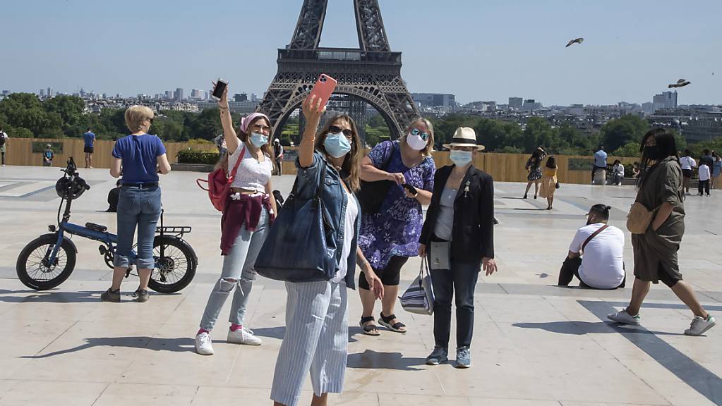 Menschen mit Mundschutzen machen Selfies vor dem Eiffelturm auf dem Trocadero-Platz. Die Pariser genießen ihr erstes Wochenende in der Sonne seit den teilweisen Lockerungen der Reise- und Bewegungsbeschränkungen. Foto: Michel Euler/AP/dpa