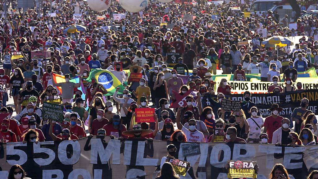 Demonstranten halten ein Banner hoch. Tausende Brasilianer sind gegen die Corona-Politik der Regierung von Bolsonaro auf die Straße gegangen. Foto: Eraldo Peres/AP/dpa