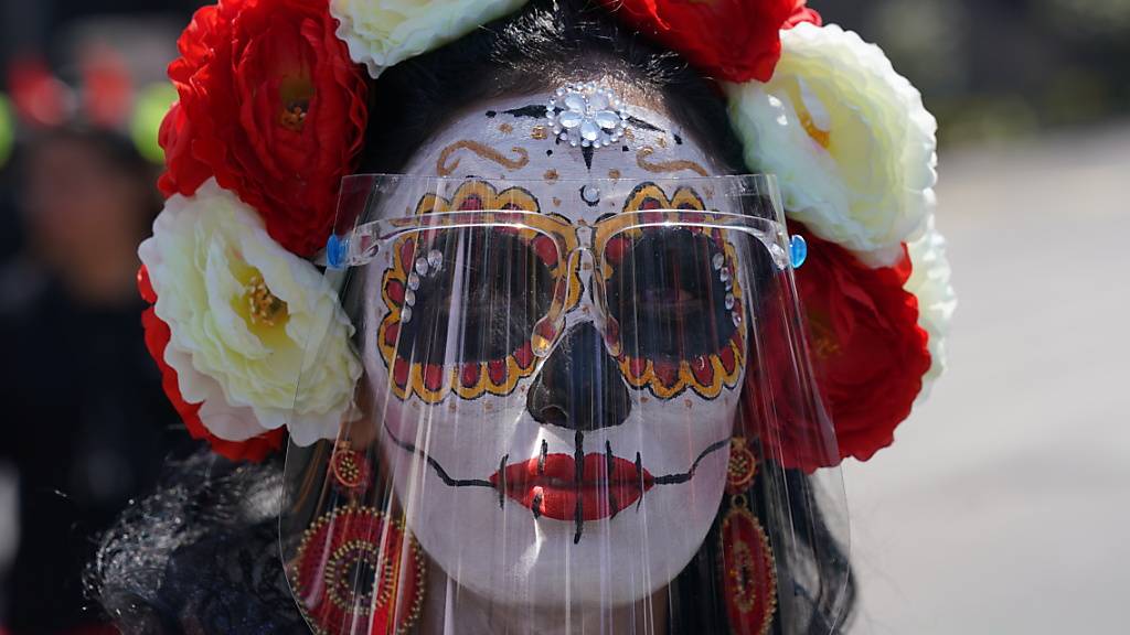 Eine als «Catrina» verkleidete Frau trägt während der Feierlichkeiten zum Tag der Toten ein Gesichtsschild. Foto: Fernando Llano/AP/dpa