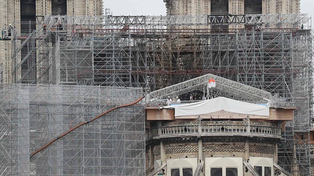 Arbeiter auf einer Plattform demontieren beschädigte Gerüstteile an der Kathedrale Notre-Dame. Foto: Ludovic Marin/AFP/dpa