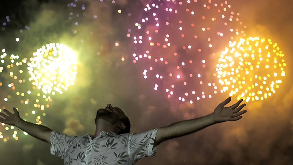 Ein Mann feiert den Beginn des neuen Jahres, während im Hintergrund ein Feuerwerk über dem Copacabana-Strand in Rio De Janeiro den Nachthimmel erleuchtet.