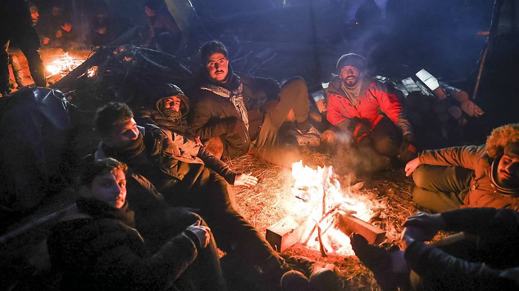 Migranten wärmen sich an einem Feuer an der weißrussisch-polnischen Grenze. Auch nach einer Woche in der Kälte warten Tausende Migranten im Grenzgebiet zwischen Polen und Belarus weiter auf Hilfe. Foto: Oksana Manchuk/BelTA/AP/dpa