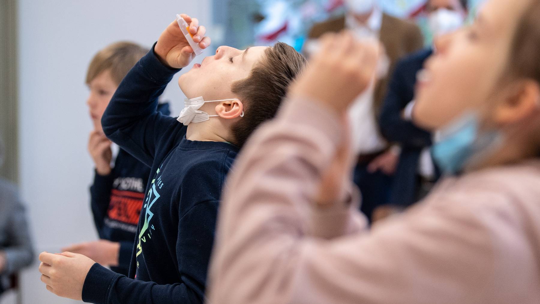 Johann (10 Jahre), Schüler einer vierten Klasse einer Grundschule, lässt sich während eines selbst durchgeführten Coronatests ein Wattestäbchen aus einem Teströhrchen in den Mund fallen. Für den Corona-Selbsttest, der als PCR-Test von einem Labor ausgewertet wird, nehmen die Schüler für einige Sekunden ein Watte-Röhrchen in den Mund, das sich während dieser Zeit mit Speichel vollsaugt. Der bayerischen Kultusminister Piazolo (Freie Wähler) und der bayerische Gesundheitsminister Holetschek (CSU) besuchen die Grundschule, um sich die Umsetzung der Corona-Teststrategie anzuschauen.