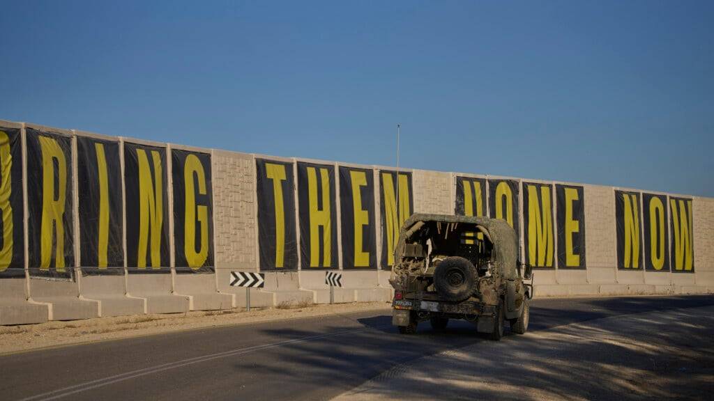 ARCHIV - Ein Fahrzeug der israelischen Armee fährt in der Nähe der Grenze zwischen Israel und Gaza vor einem Transparent mit der Aufschrift «Bring them home now», auf dem die Freilassung von Geiseln gefordert wird. Foto: Ohad Zwigenberg/AP/dpa/Archivbild