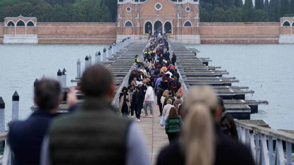 Menschen gehen über die Brücke, die Venedig mit dem Friedhof auf der Insel San Michele verbindet. Foto: Luca Bruno/AP/dpa