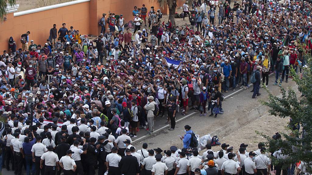 Migranten aus Honduras stehen vor Polizisten, die eine Straße blockieren. Foto: Sandra Sebastian/AP/dpa