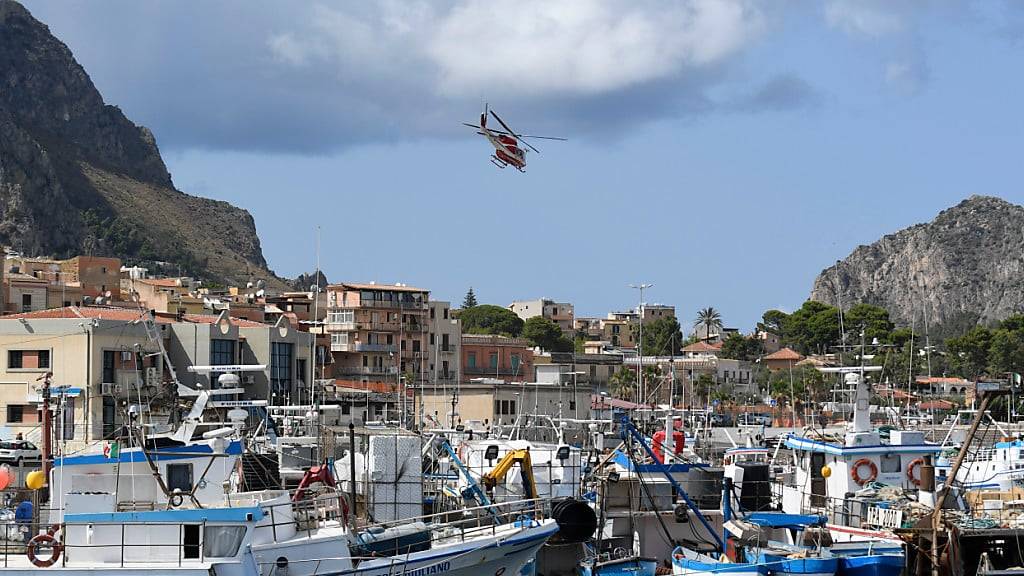 Ein italienischer Feuerwehrhubschrauber fliegt über den Hafen von Porticello. Foto: Salvatore Cavalli/AP/dpa