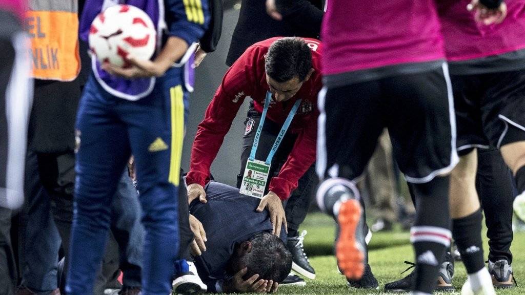 Besiktas-Coach Senol Günes krümmt sich nach dem Messerwurf vor Schmerz auf dem Rasen.