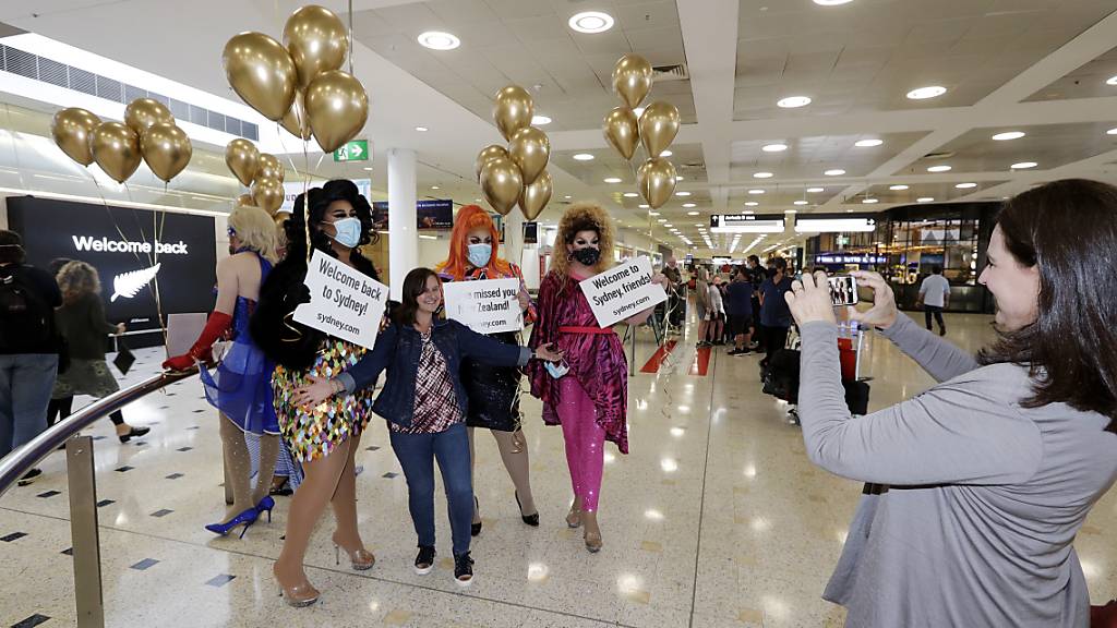 Eine Passagierin aus Neuseeland (M) stellt sich mit sich für ein Foto mit Drag Queens, die sie am Flughafen Sydney begrüßen, auf. Erstmals seit Beginn der Corona-Pandemie können Menschen in Neuseeland und Australien ab dem 19. April wieder zwischen beiden Ländern reisen.