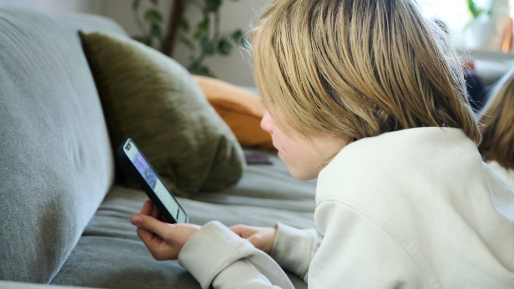 ARCHIV - Ein Junge liegt auf einem Sofa und guckt auf sein Smartphone. Foto: Annette Riedl/dpa