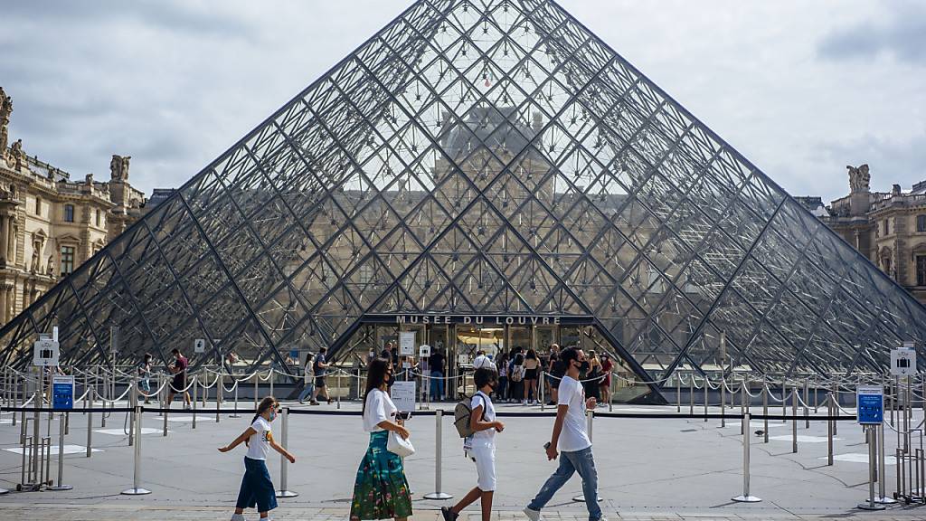 ARCHIV - Eine Familie mit Schutzmasken geht am Louvre vorbei. (zu dpa «Corona-Krise: Frankreich kommt seinen großen Museen zu Hilfe») Foto: Kamil Zihnioglu/AP/dpa