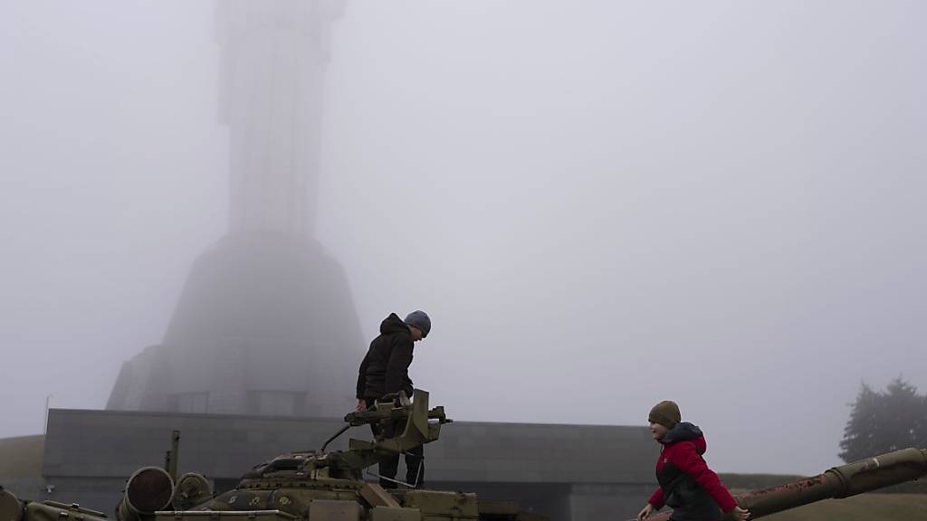 Zwei Jungen spielen auf einem als Denkmal aufgestellten Panzer vor dem Denkmal Mutter Ukraine. Foto: Alex Babenko/AP/dpa
