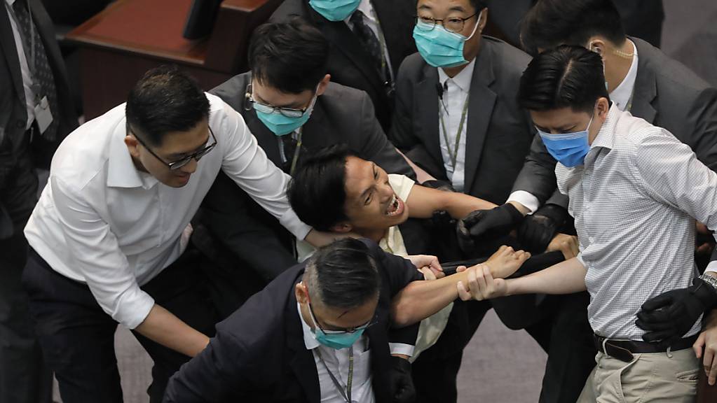 Eddie Chu Hoi-Dick (M), Mitglied des Legislativrates, wird von Sicherheitskräften abgeführt, nachdem es während einer Ausschusssitzung des Legislativrats zu Auseinandersetzungen zwischen den Teilnehmern kam. Foto: Vincent Yu/AP/dpa
