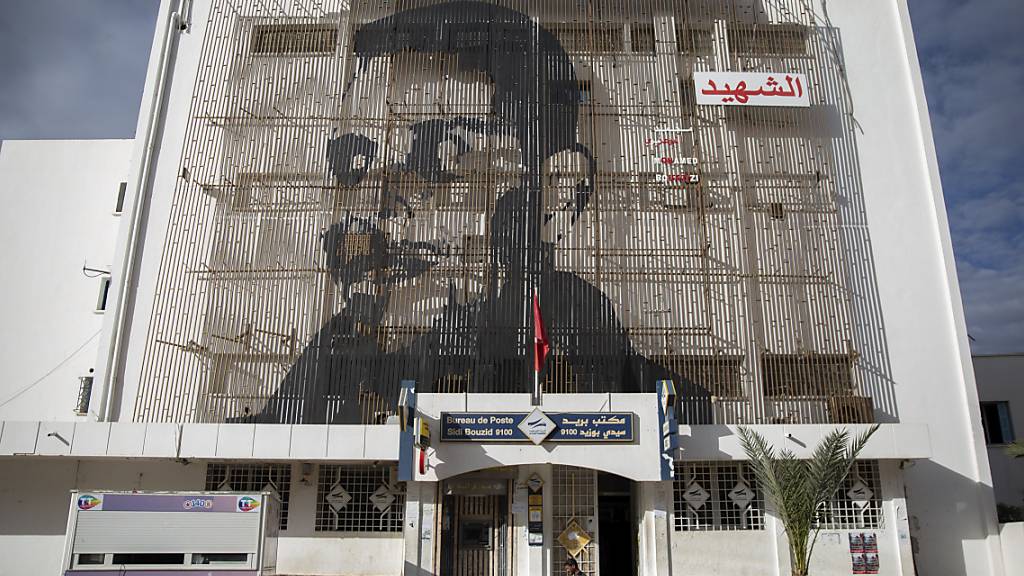 ARCHIV - Auf der Fassade eines Postamtes in der tunesischen Kleinstadt Sidi Bouzid ist das Gesicht des tunesischen Gemüsehändlers Mohammed Bouazizi abgebildet, der sich am 17. Dezember 2010 selbst anzündete - aus Verzweiflung über seine Lebenslage und die Willkür der Behörden. Foto: Riadh Dridi/AP/dpa
