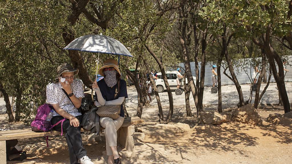 ARCHIV - Touristen sitzen unter Bäumen am Eingang der Akropolis im Zentrum von Athen. Der Juli 2023 dürfte mit größter Wahrscheinlichkeit der bislang heißeste Monat seit Messbeginn werden. Foto: Socrates Baltagiannis/dpa