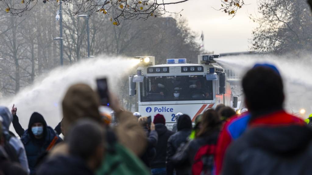 Protestteilnehmer filmen mit ihren Telefonen, wie die Polizei bei einem Zusammenstoß mit Demonstranten Wasserwerfern einsetzen. Nach Angaben der Polizei protestierten am Sonntag rund 35 000 Menschen in Brüssel gegen die verschärften Corona-Maßnahmen und insbesondere den Corona-Pass in Belgien. Foto: Hadrien Dure/BELGA/dpa