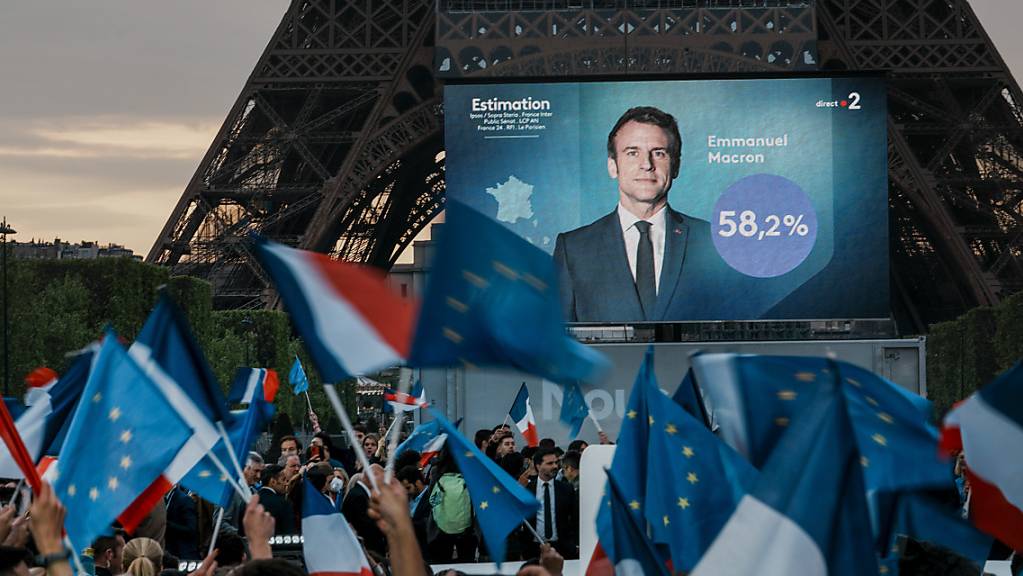 Emmanuel Macron, Präsident von Frankreich, ist auf einem Bildschirm vor dem Eiffelturm zu sehen, als die ersten Wahlprognosen bekannt gegeben werden. Der Liberale Macron ist Hochrechnungen zufolge als französischer Präsident wiedergewählt worden. Foto: Christophe Ena/AP/dpa