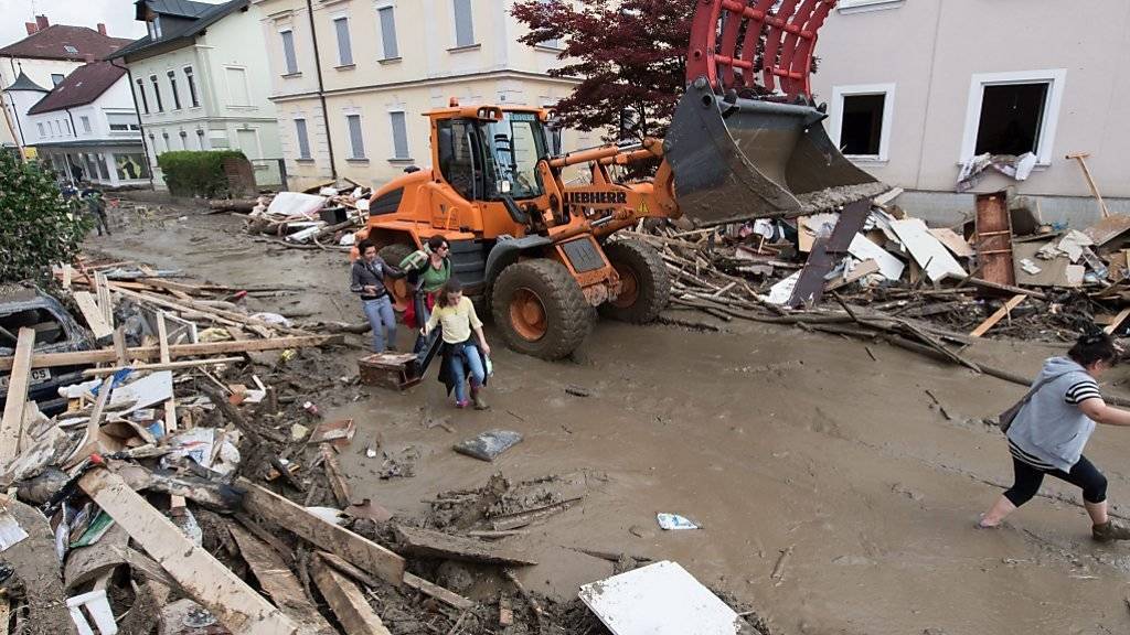 Ein Bagger und Anwohner in einer mit Schlamm bedeckten Strasse in Simbach am Inn.