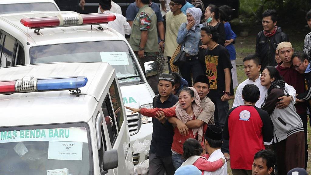 Angehörige brechen in Tränen aus, als Ambulanzen mit den Opfern des Busunfalles im Heimatdorf im indonesischen East Ciputat eintreffen.
