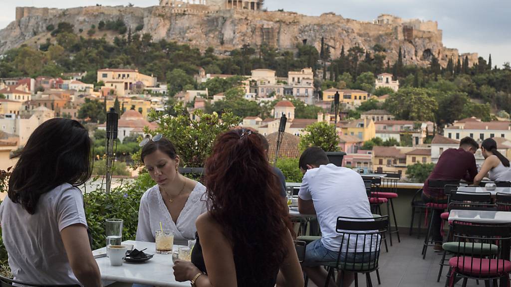 ARCHIV - Ab Montag wieder möglich: Gäste sitzen in einem Cafe in Athen mit der Akropolis im Hintergrund. (Archivbild) Foto: Socrates Baltagiannis/dpa