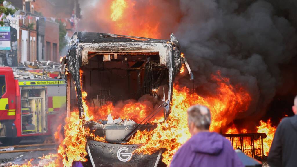 dpatopbilder - Menschen beobachten, wie ein Fahrzeug während einer Demonstration in East Belfast nach einem Messerangriff in Belfast brennt. Foto: Peter Morrison/AP/dpa