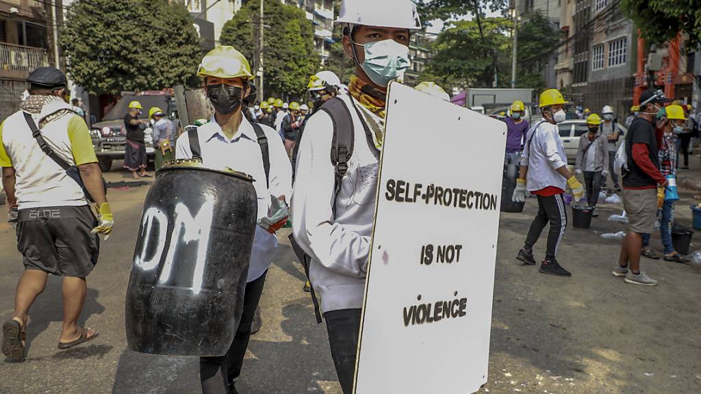 Anti-Putsch-Demonstranten mit Helmen halten währende eines Protests behelfsmäßige Schilder mit der Aufschrift «Self protection is not violence» (Selbstschutz ist keine Gewalt). Foto: Str/AP/dpa