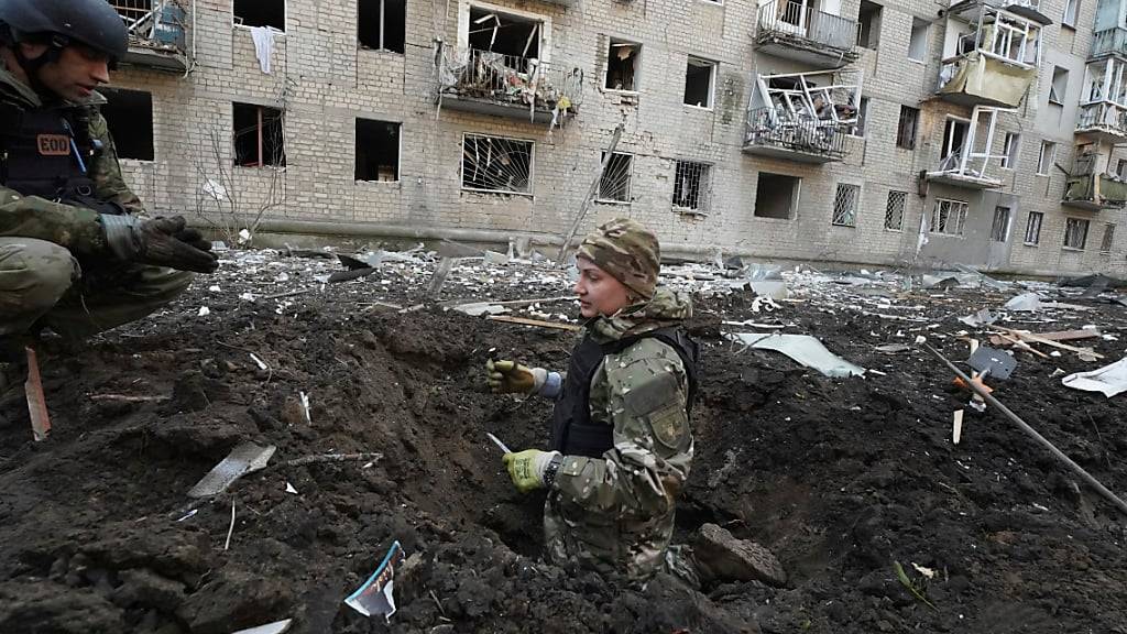 Polizeibeamte inspizieren einen Krater vor einem beschädigten Wohnhaus, das bei einem russischen Angriff getroffen wurde. Foto: Andrii Marienko/AP/dpa