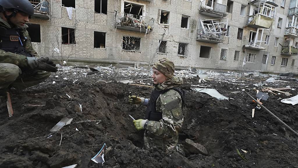 Polizeibeamte inspizieren einen Krater vor einem beschädigten Wohnhaus, das bei einem russischen Angriff getroffen wurde. Foto: Andrii Marienko/AP/dpa