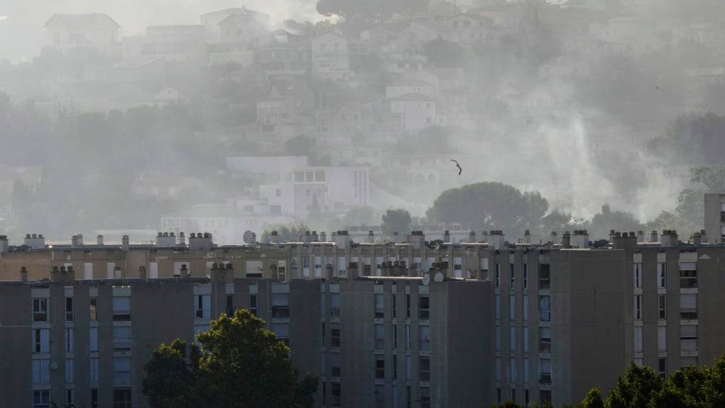 Rauch steigt hinter Gebäuden im Stadtteil La Castellane während eines Waldbrandes. Nach der Hitzewelle der vergangenen Woche sind in Südfrankreich an etlichen Orten Naturbrände ausgebrochen. Foto: Lewis Joly/AP/dpa
